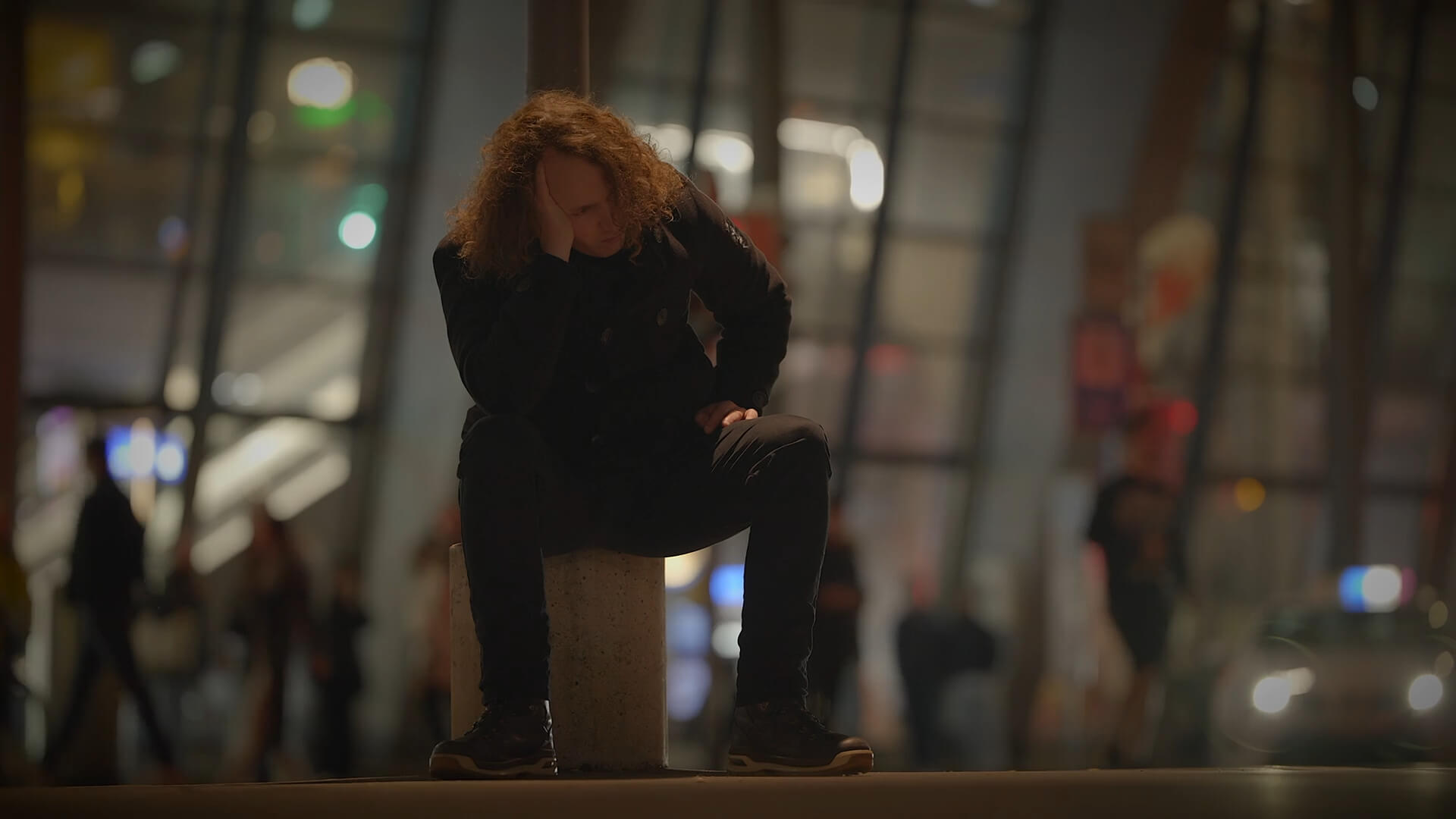 Guy sitting on a concrete post on the street